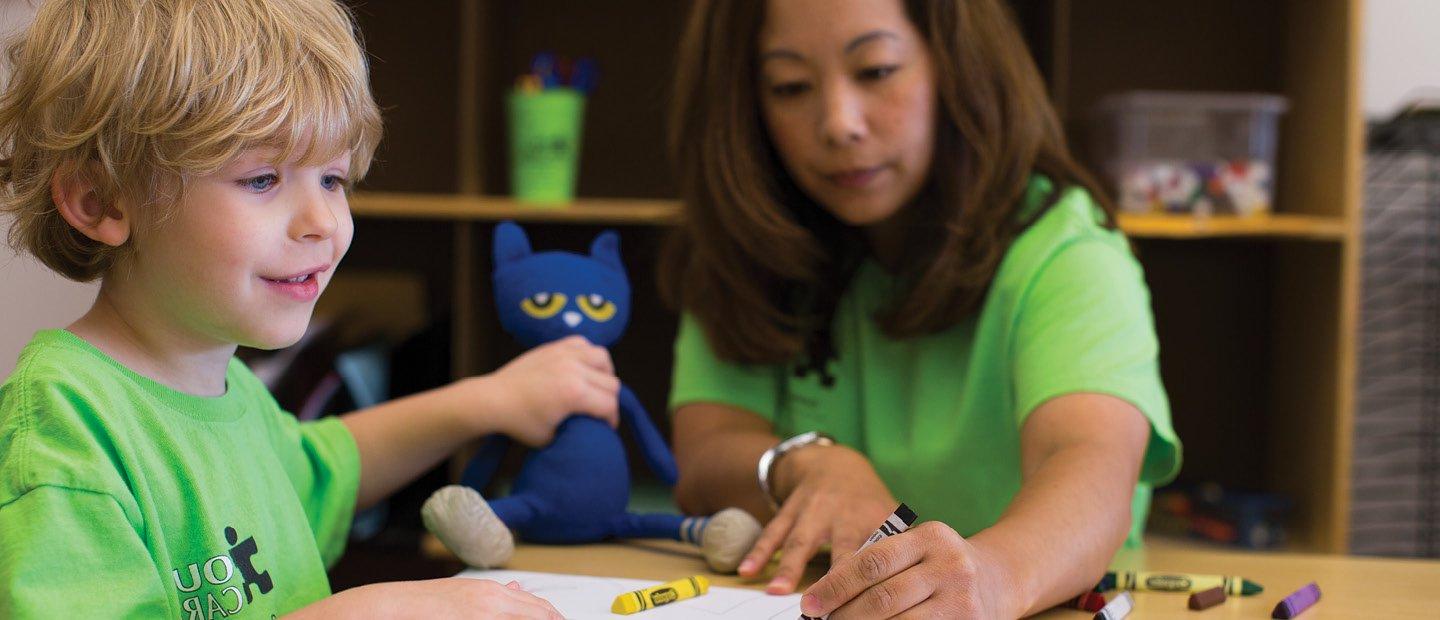 Woman and young child in bright green shirts, coloring with crayons.