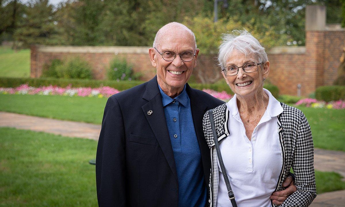 Barbara and Roger Calam, Ph.D. stand smiling in a garden next to each other.